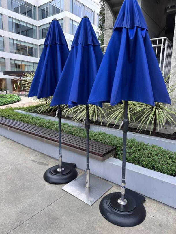 Commercial-grade blue patio umbrellas in immaculate condition, heavy-duty design, ready for use, on sturdy bases.