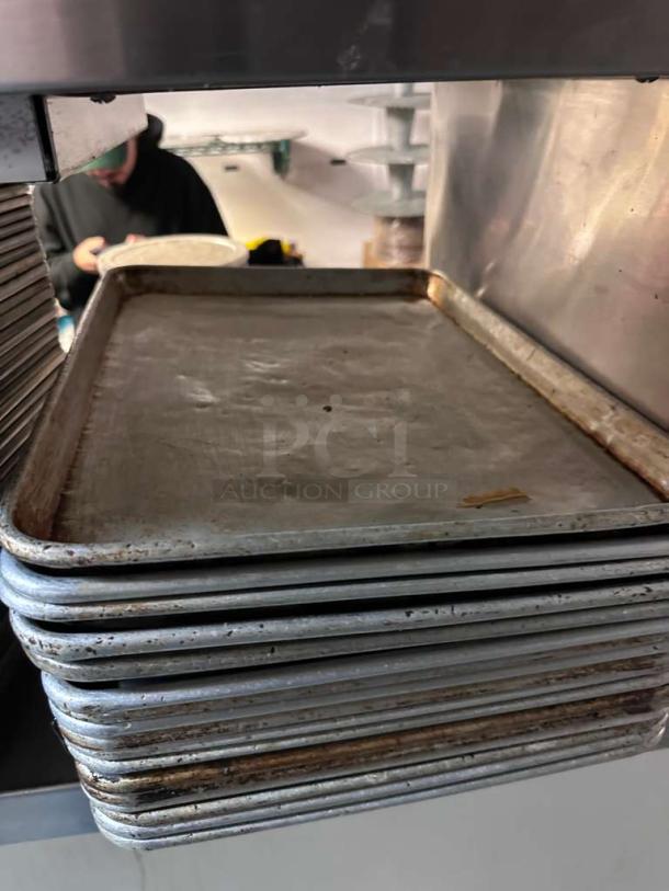 Eighteen commercial-grade aluminum half sheet pans in outstanding condition, stacked neatly, fully functional.