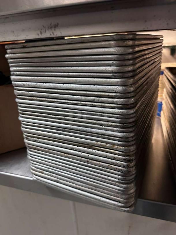 Stack of 36 commercial-grade aluminum 1/4 sheet pans, premium condition, ready for use, on a metal shelf.