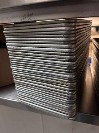 Stack of 36 commercial-grade aluminum 1/4 sheet pans, premium condition, ready for use, on a metal shelf.