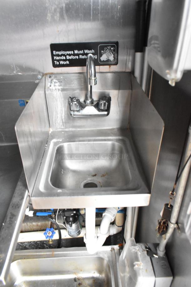Stainless steel sink in a food trailer kitchen with hand wash sign visible. Fixtures appear in good condition.
