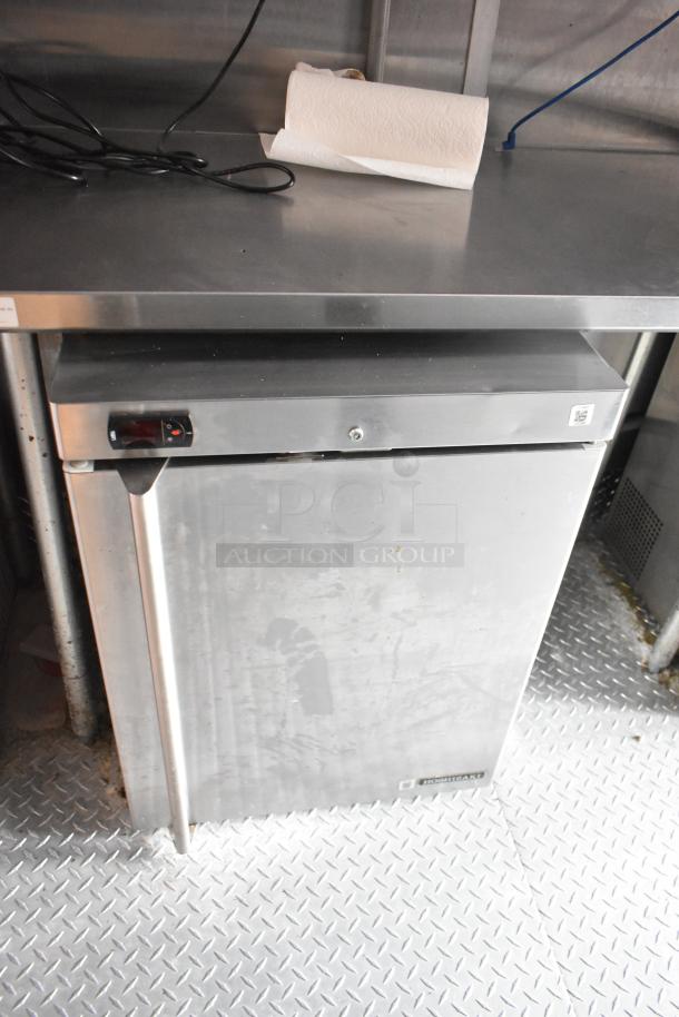 Stainless steel commercial cooler in food trailer, featuring a Hoshizaki logo on the door, clean and functional.