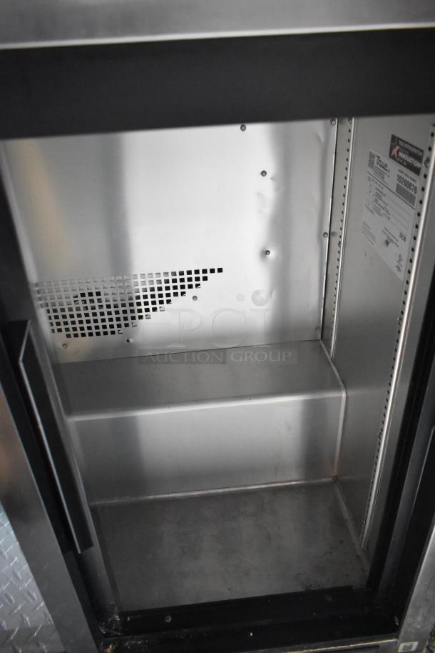 Stainless steel interior of a True merchandiser cooler, showing clean metal walls and labeling for model and specifications.