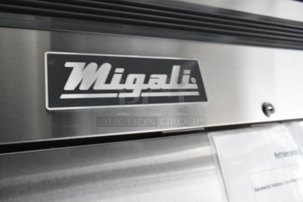 Close-up of a Migali logo on stainless steel equipment, possibly part of a commercial kitchen appliance in a fast food trailer.