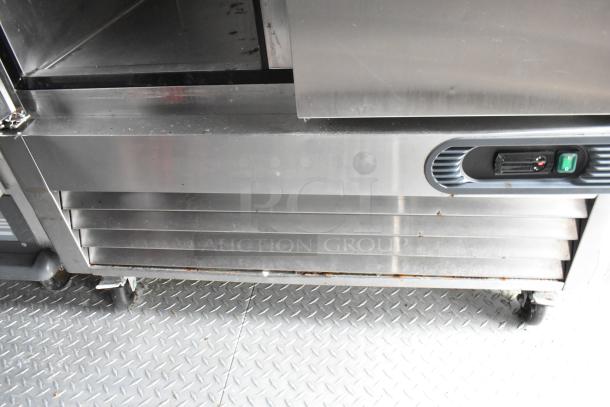 Stainless steel kitchen appliance in fast food trailer, featuring vented front panel and green power switch, in used condition.