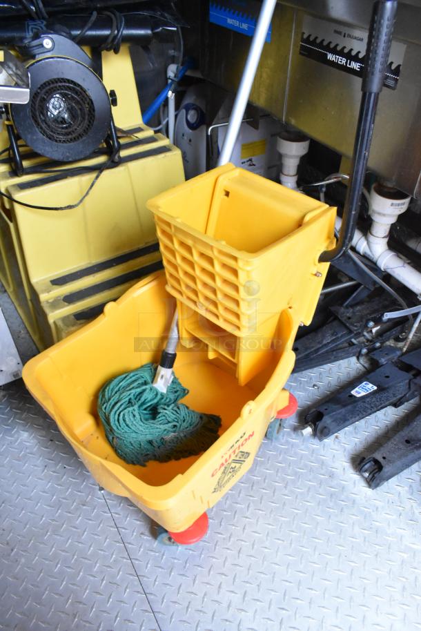 Yellow mop bucket with a green mop inside, set on a metal floor inside the 28' Wendy's fast food trailer kitchen.