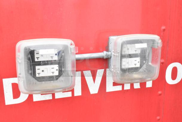 Red fast food trailer exterior showing two outdoor electrical outlets with protective covers. Text reads "DELIVER."
