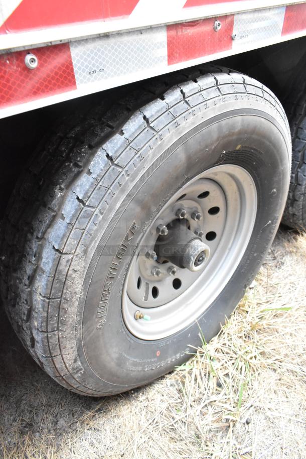 Close-up of a Westlake tire on a Wendy's fast food trailer, showing tread detail and metal rim. Reflective strip above.