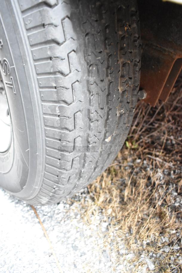 Close-up of Rock Solid Cargo trailer tire on gravel, showing significant tread wear. Suitable for inspection.