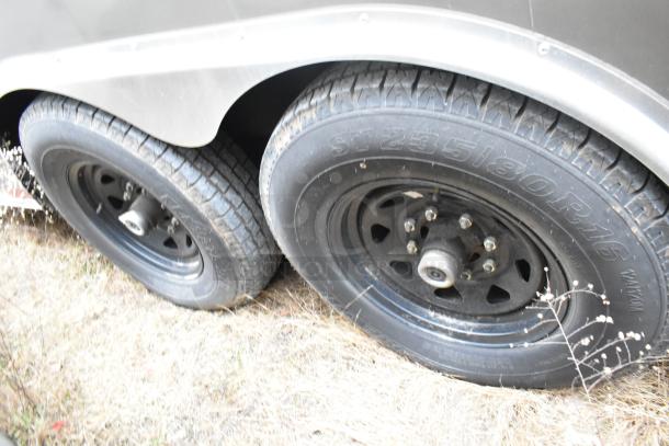 Close-up of dual wheels on a Nationwide 24' food trailer, black rims, tires marked ST235/80R16, grassy ground.