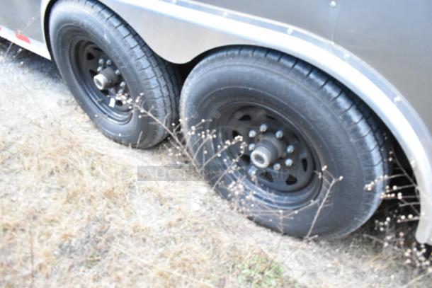 Dual axle wheels of Nationwide 24' food trailer, showing black rims and tires on grassy terrain.
