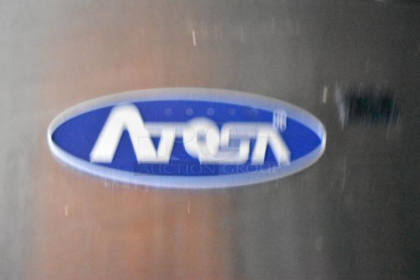 Blurred Atosa logo on a stainless steel surface, indicating inclusion of Atosa equipment in Stuff4less mobile kitchen trailer.