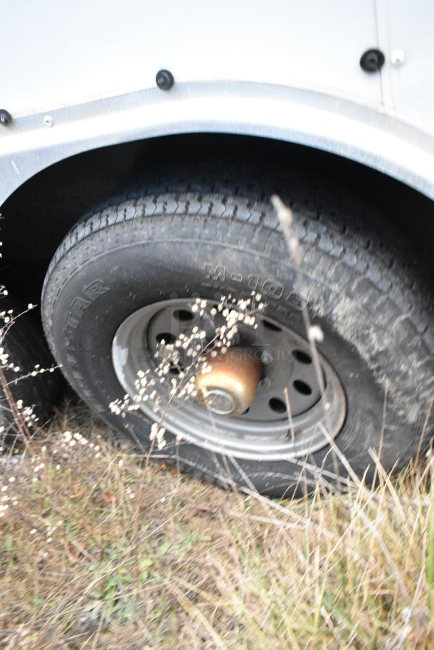 Close-up of trailer wheel from a Stuff4less 24' fast food trailer, showing tire and rim in outdoor setting.