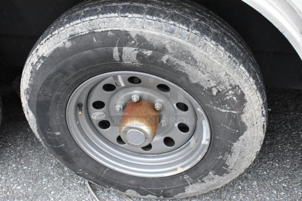 Wheel of Stuff4less 24' mobile kitchen trailer, showing wear and rust on rim, ready for customization and outfitting.