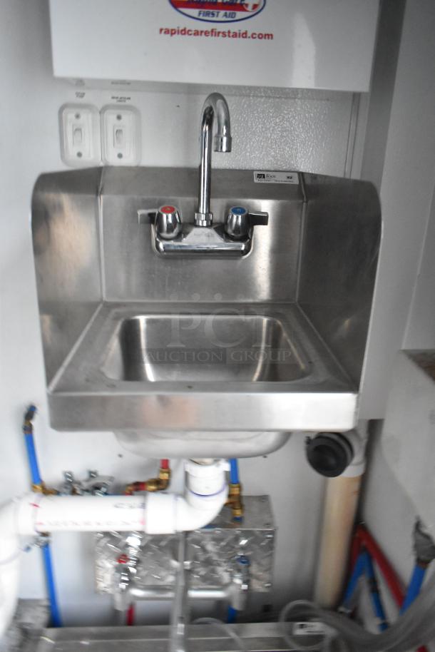 Stainless steel hand sink with hot and cold faucets in SDG 20' food trailer. Visible plumbing and labeled Rapid Care First Aid.