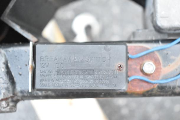 Breakaway switch labeled "12V DC" with caution and warning text, mounted on metal surface with blue wires attached.
