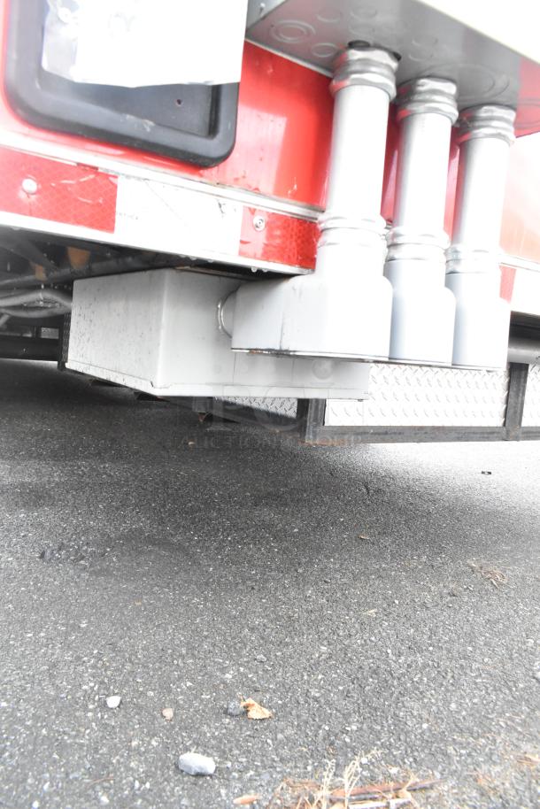 Undercarriage view of a red Rock Solid Cargo mobile kitchen trailer with visible piping, on asphalt surface.