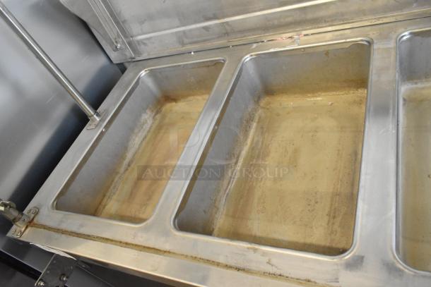 Stainless steel 4-well heated buffet station with tray slide and glass overshelf; visible wear indicates used condition.