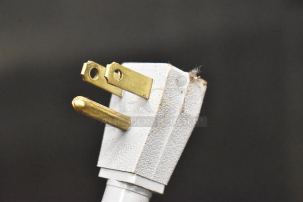 Close-up of a white electrical plug with three prongs, visible wear on the surface, related to a commercial appliance.
