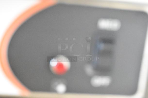 Blurred control panel of a Nemco 6311-4-240 stainless steel electric hot plate. Features include a red indicator light.