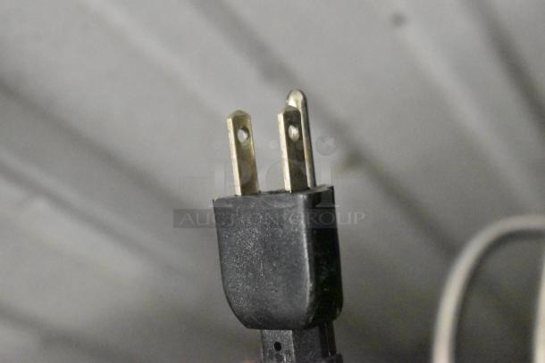 Close-up of a black electrical plug with two parallel prongs and a grounding pin, compatible with 115 volts.