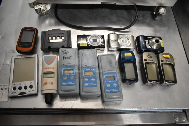 15 assorted items including digital cameras, Garmin GPS units, and Hach colorimeters on a metal surface; various conditions.