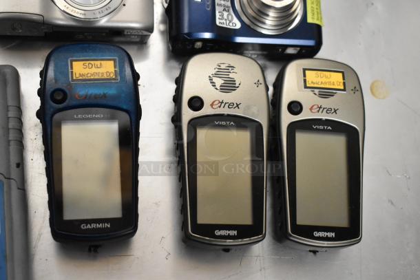 Assorted electronics including Garmin eTrex GPS units and digital cameras, some with visible label marks.