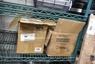 Two boxes on a shelf, one labeled "Acopa Pangea Blue 15 oz. Stemless Wine Glass" and the other "Acopa Keystone 10 oz. Stoneware Creamer". Both boxes indicate 12 per case. Item condition: new, scratch and dent.