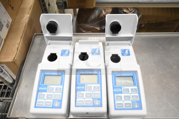 Three Hach 2100P turbidimeters on a metal shelf, used condition, showing control panels and open sample compartments.