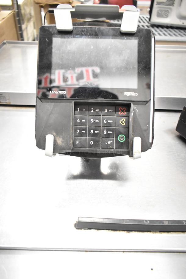 Ingenico Lane/7000 card reader with numeric keypad, visible signs of wear, shown on a metallic surface.
