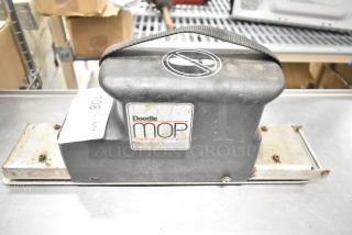 Doodlemop 36 VDC scrub battery with handle, showing wear and rust on metal parts. Visible logo and caution symbol.