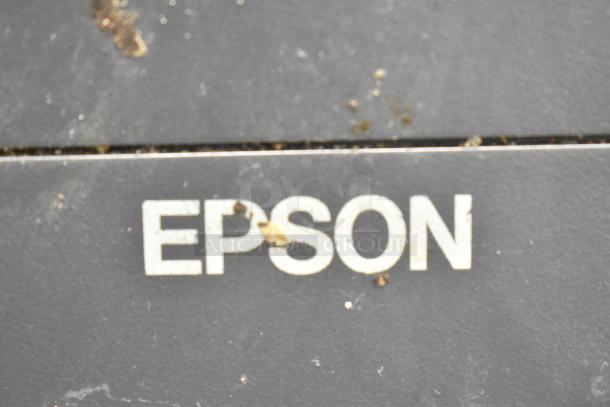 Epson M313A receipt printer close-up with visible logo on dusty surface, indicating usage wear.
