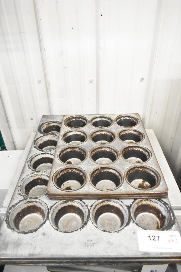 Seven metal muffin baking pans, including 12-cup and 20-cup models, show signs of wear. Auction tag "127 QTY VX1" visible.