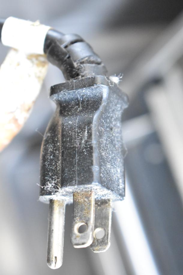 Close-up of a black electrical plug. Dust is visible on its surface. It is part of the Hatco GRMW-3 warming display.