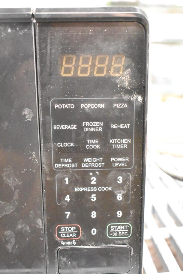 Black countertop microwave oven model MSF0B100072352 with digital display and touchpad controls. 120 volts, 1 phase. Visible wear.