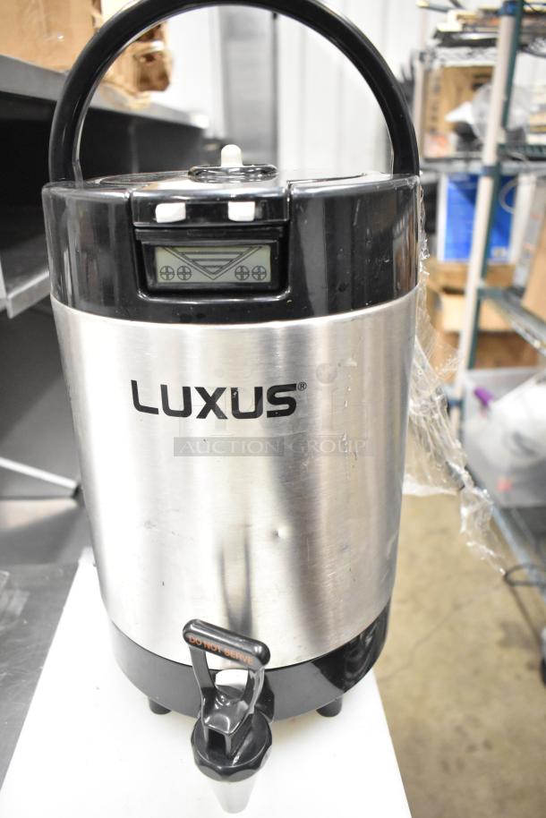 Luxus stainless steel beverage dispenser with spigot, digital panel, and carrying handle, minor dents visible.