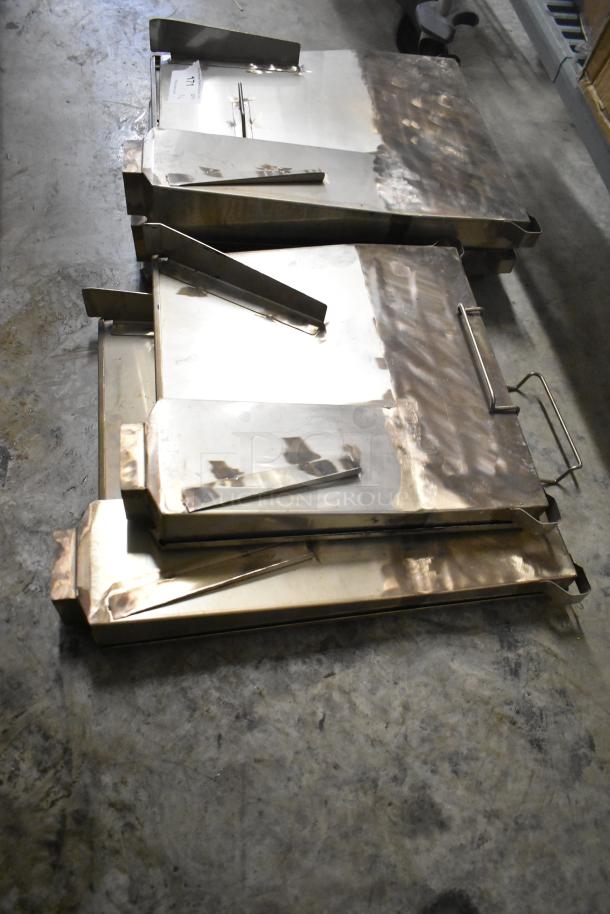 Six metal oven pieces with handles, slightly tarnished, stacked on a concrete floor. Auction label visible.