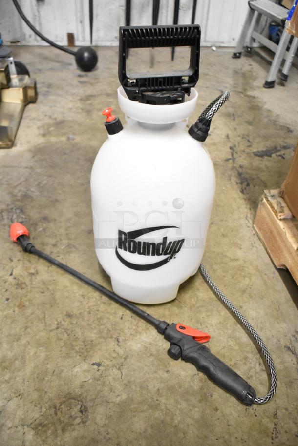 Roundup sprayer with black handle and hose, in good condition, featuring logo on white tank, resting on concrete floor.