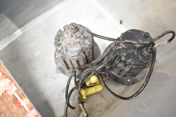 Two black, used motors with visible wiring and dirt, possibly for industrial or gardening use. No identifiable labels.