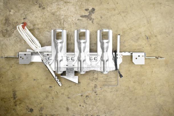 Three metal burner components with wiring and brackets on a workshop floor. New condition. Includes mounting hardware.