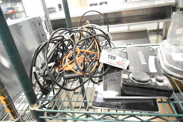 Assorted auction items: Netgear box, Verifone reader, Apple iPad, Astro Mixamp, Windows tablet. Includes tangled cables. Lot tag visible.