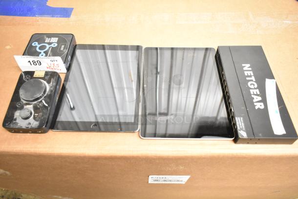 Netgear box, Verifone credit card reader, Apple iPad, Astro MixAmp, Windows tablet on cardboard box. Condition visible.