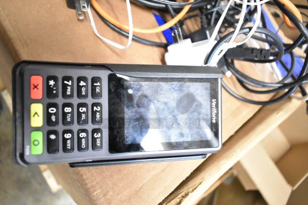 Verifone credit card reader with numeric keypad and display screen, resting atop cables and box, indicating part of a 5-item auction lot.