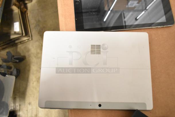 Five-item auction lot featuring Netgear box, Verifone reader, Apple iPad, Astro Mixamp, and Windows tablet; mixed condition.