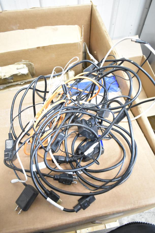 Box with assorted cables for electronic devices, alongside packaging materials. Items include a variety of power and data cords.