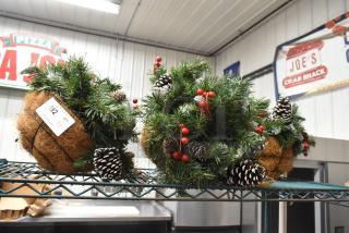 Three decorative fake plants with pine needles, red berries, and pinecones in coco fiber baskets. Auction lot tag: 192, Qty: 3.