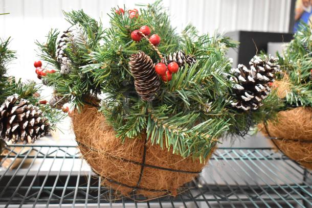 Three artificial plants in round coconut fiber baskets, adorned with faux pine cones and red berries, in excellent condition.