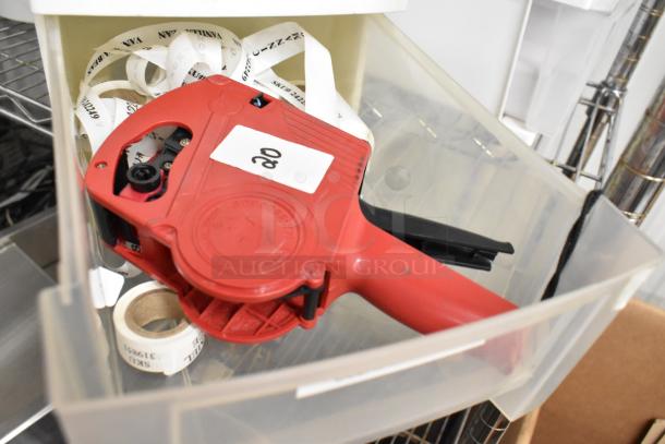Red label maker in a clear poly bin with rolls of labels and a plastic handle, part of a tier lot auction.