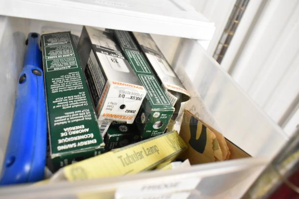 Tiered lot of items including Sylvania light bulb boxes, GE tubular lamp box, and a blue tool inside a poly bin.