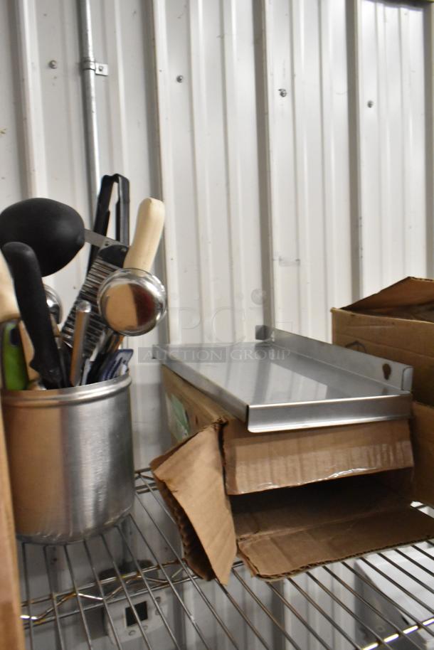 Tiered auction lot featuring a stainless steel utensil holder, assorted utensils, metal panel, and cardboard box, in good condition.